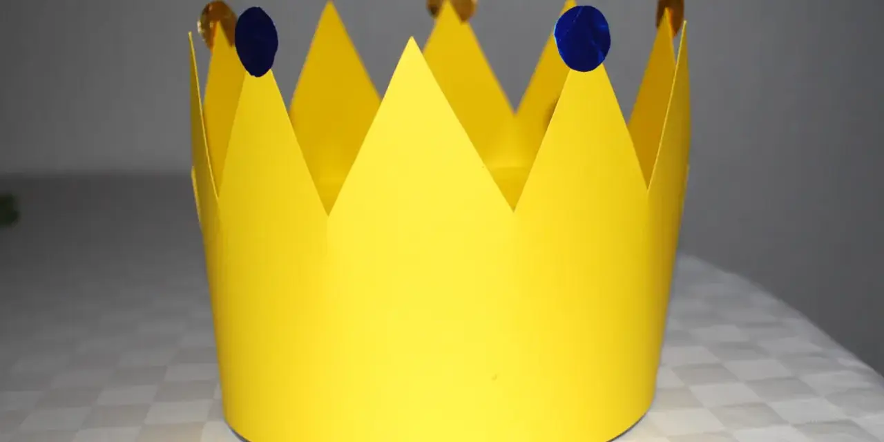 Gelbe Papierkrone, die zum **krone basteln** einlädt. Mit blauen Tupfern und goldenen Münzen verziert, wartet sie auf ihren kleinen König oder ihre kleine Königin.