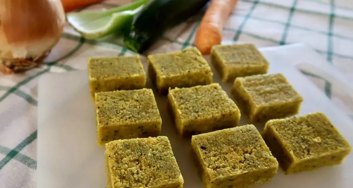 Cubetti di dado vegetale fatto in casa, pronti per insaporire le tue ricette. Sullo sfondo, ingredienti freschi come carote, zucchine e cipolla.