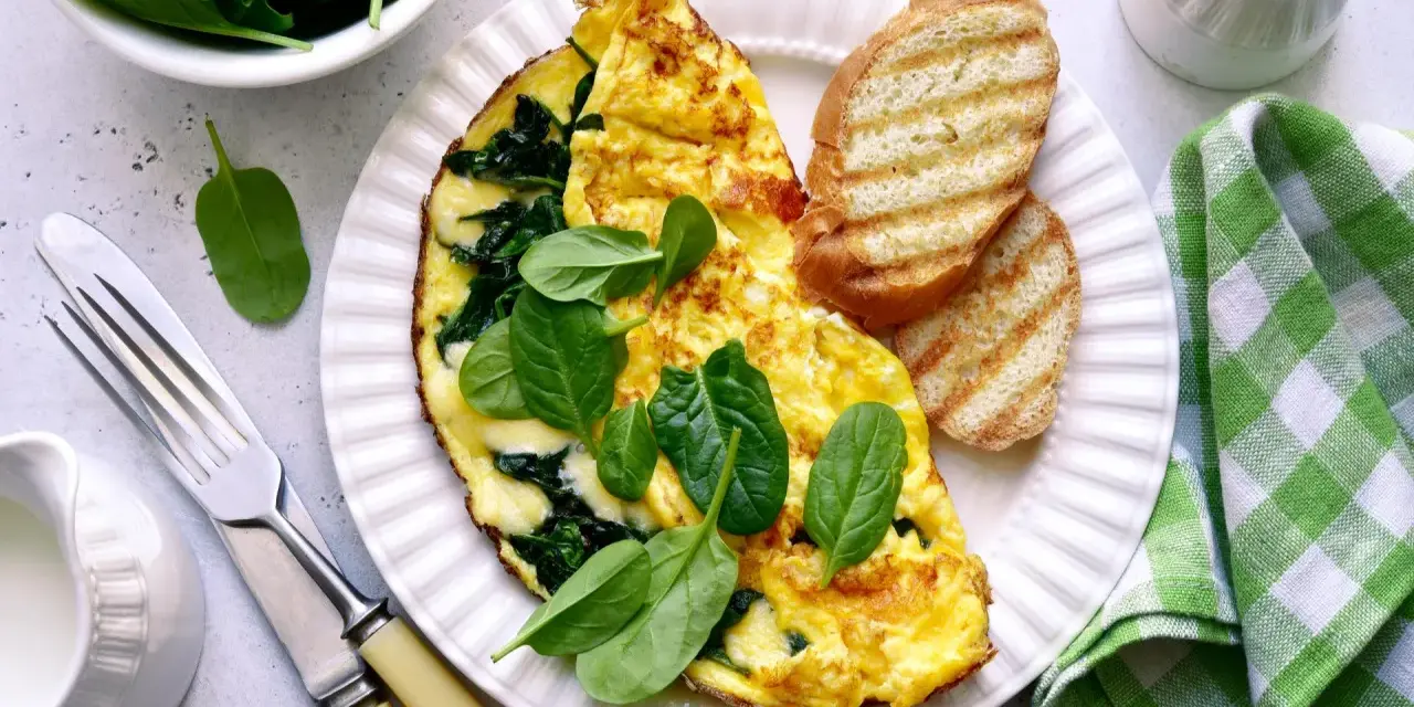 Pyszny omlet ze szpinakiem, podany z grzankami i świeżymi liśćmi szpinaku. Idealne śniadanie pełne witamin.