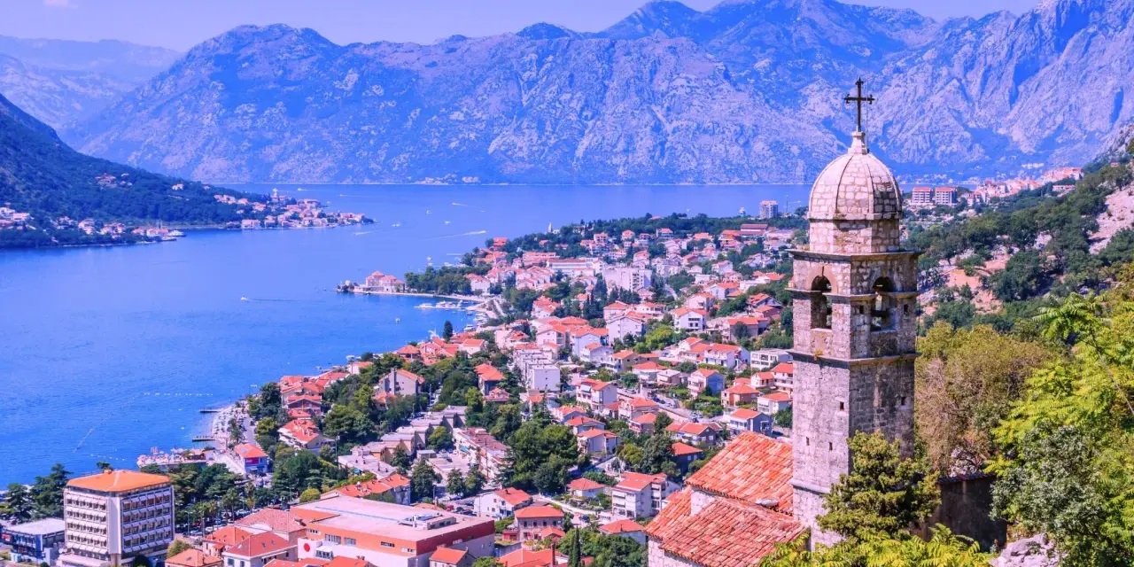 Vista panoramica delle Bocche di Cattaro, con un campanile in primo piano e montagne sullo sfondo.