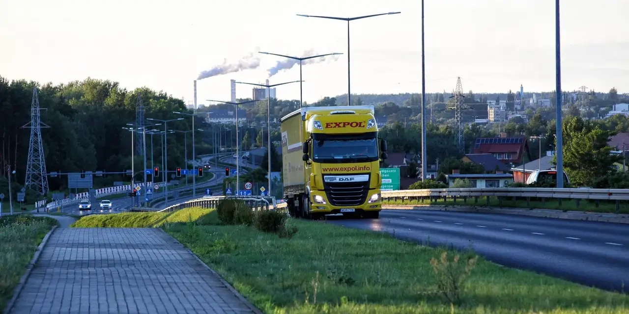 Żółta ciężarówka EXPOL jedzie drogą, symbolizując mobilność i wyzwania związane z pakietem mobilności a umową zlecenie.