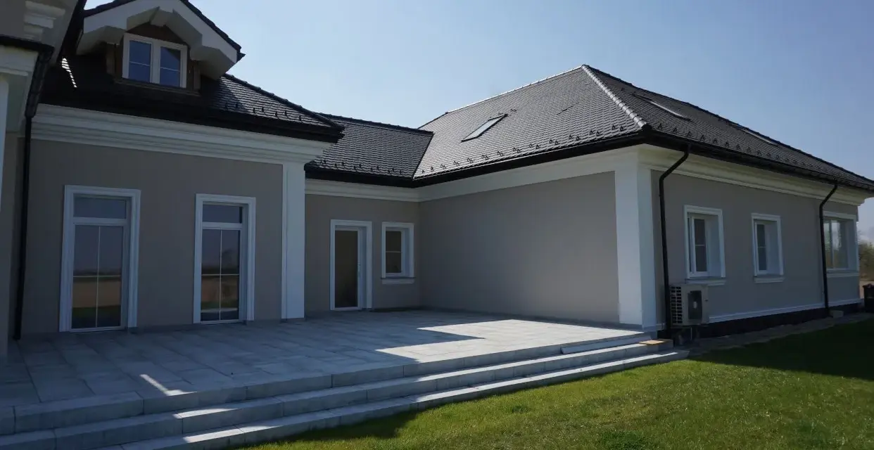 Nowoczesny dom z tarasem i trawnikiem. Elegancki gzyms podkreśla architekturę budynku.