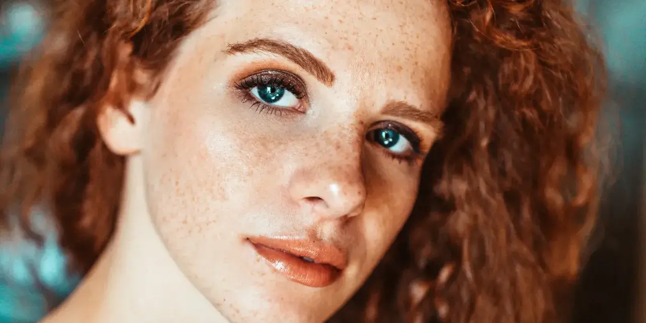 Primo piano di una ragazza con lentiggini e capelli rossi, con un trucco naturale che esalta la sua bellezza.