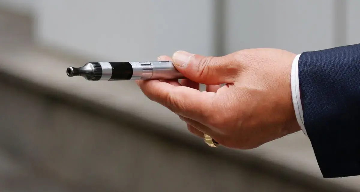 Mano con traje sosteniendo un cigarrillo electrónico, listo para vapear en el trabajo.