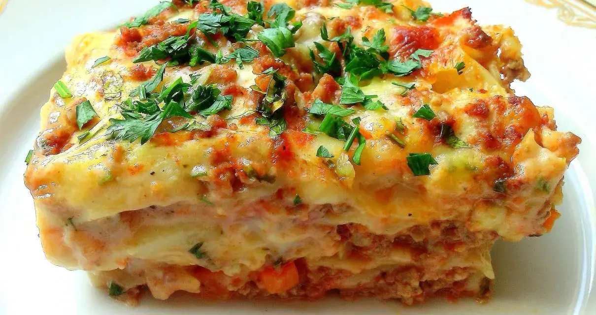 Pyszna lasagne Ani Starmach, z warstwami mięsa, sosu i sera, posypana świeżą natką pietruszki.