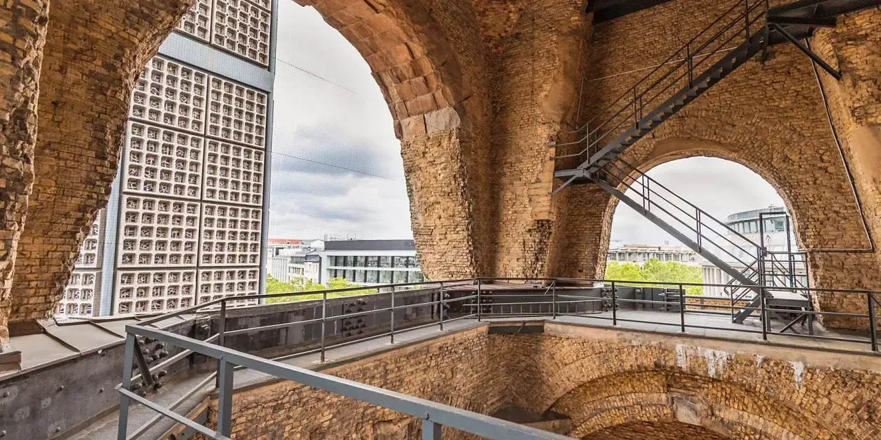 Blick durch die Bögen der Kaiser-Wilhelm-Gedächtniskirche auf eine moderne Glasfassade und Treppen.