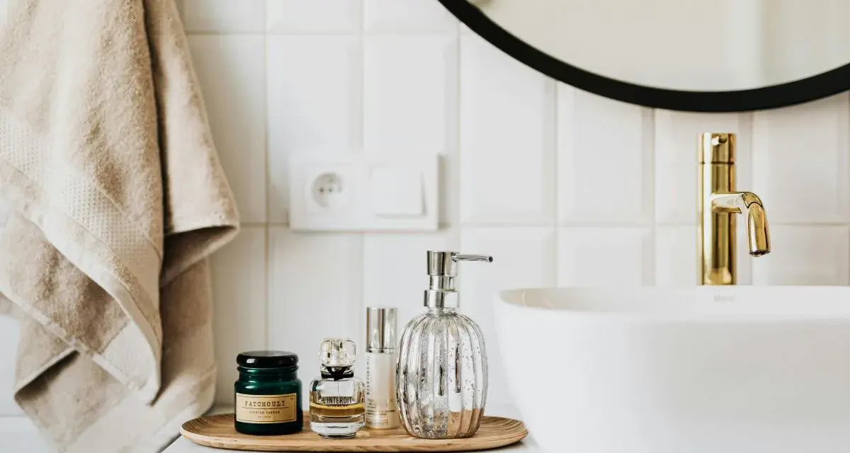 Sur un plateau en bois, des flacons de parfum et un distributeur de savon argenté. Une serviette beige est suspendue à côté d'un lavabo blanc et d'un robinet doré. La colle carrelage flex, c'est quoi ?