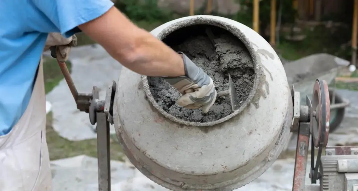 Mieszanie betonu w betoniarce. Pracownik w rękawicach sprawdza konsystencję, zastanawiając się, ile cementu na metr sześcienny betonu potrzeba do uzyskania idealnej mieszanki.