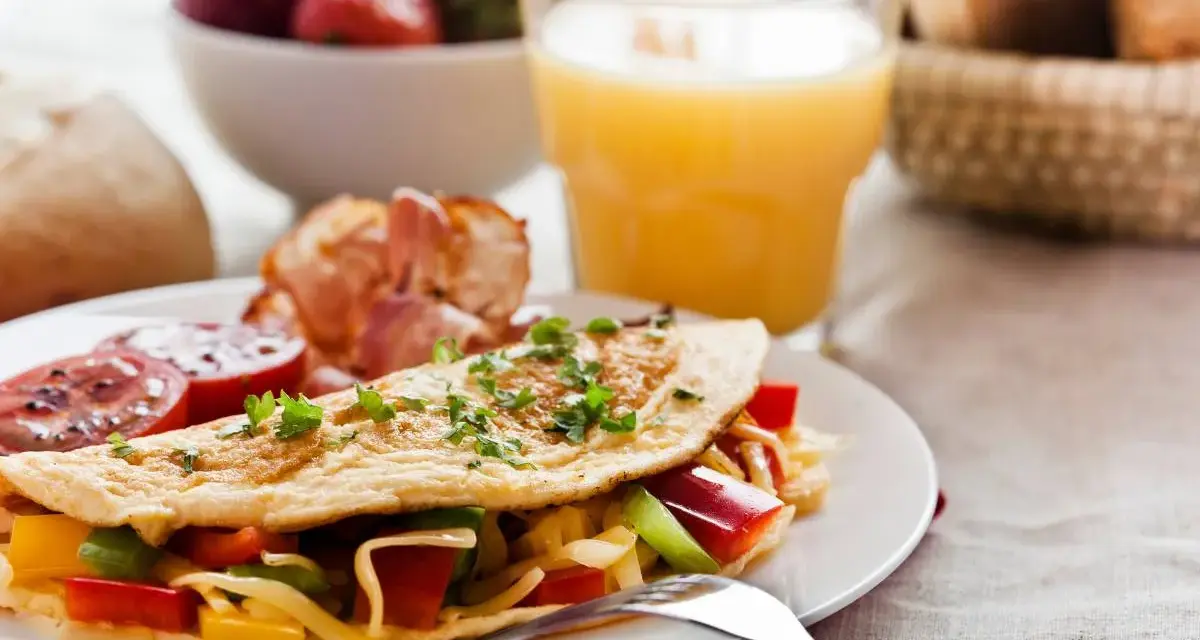 Pyszne śniadanie bez chleba: omlet z warzywami i serem, bekon, pomidory, truskawki i sok pomarańczowy.