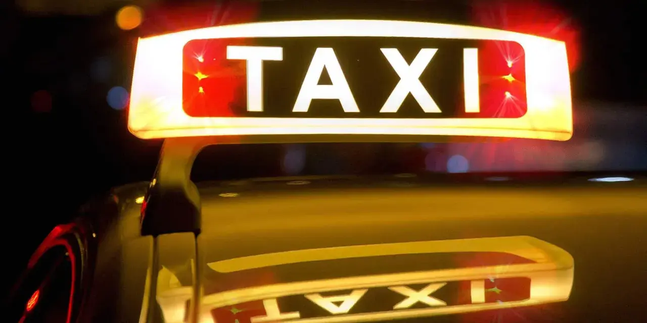 Leuchtendes TAXI-Schild mit roten Blinklichtern, das einen Taxi-Alarm signalisiert. Die Reflexion auf dem dunklen Auto verstärkt die nächtliche Atmosphäre.