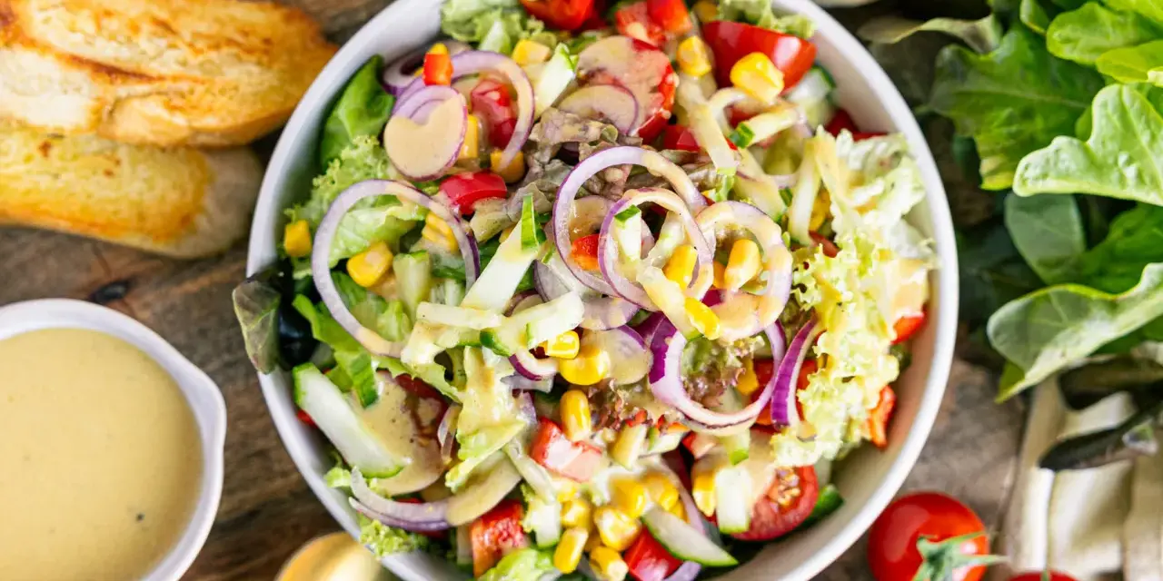 Ein bunter gemischter Salat mit knackigem Salat, Tomaten, Gurken, Mais und roten Zwiebeln, serviert mit Dressing und geröstetem Brot.