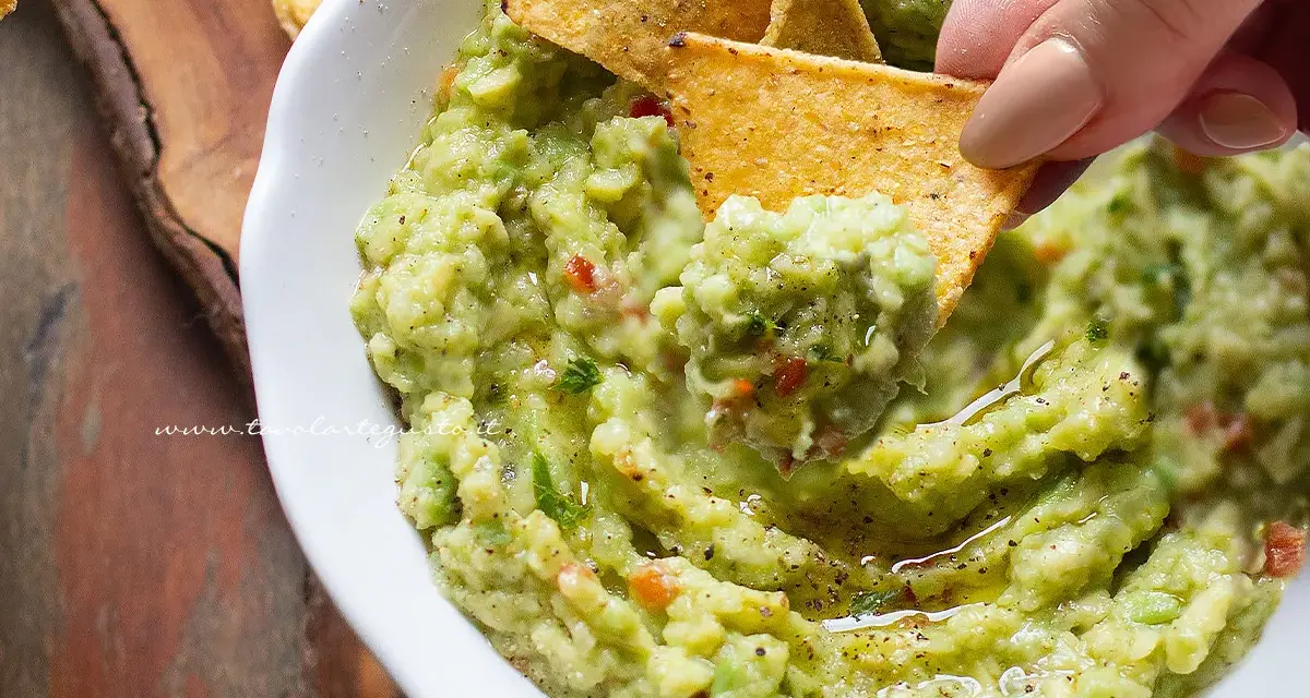 Un chip di mais raccoglie il cremoso guacamole, mostrando come fare il guacamole fresco e delizioso.