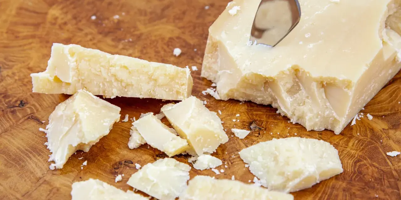 Kawałki sera Grana Padano na drewnianej desce. Czy Grana Padano to parmezan? Ten twardy ser dojrzewa długo, podobnie jak parmezan.
