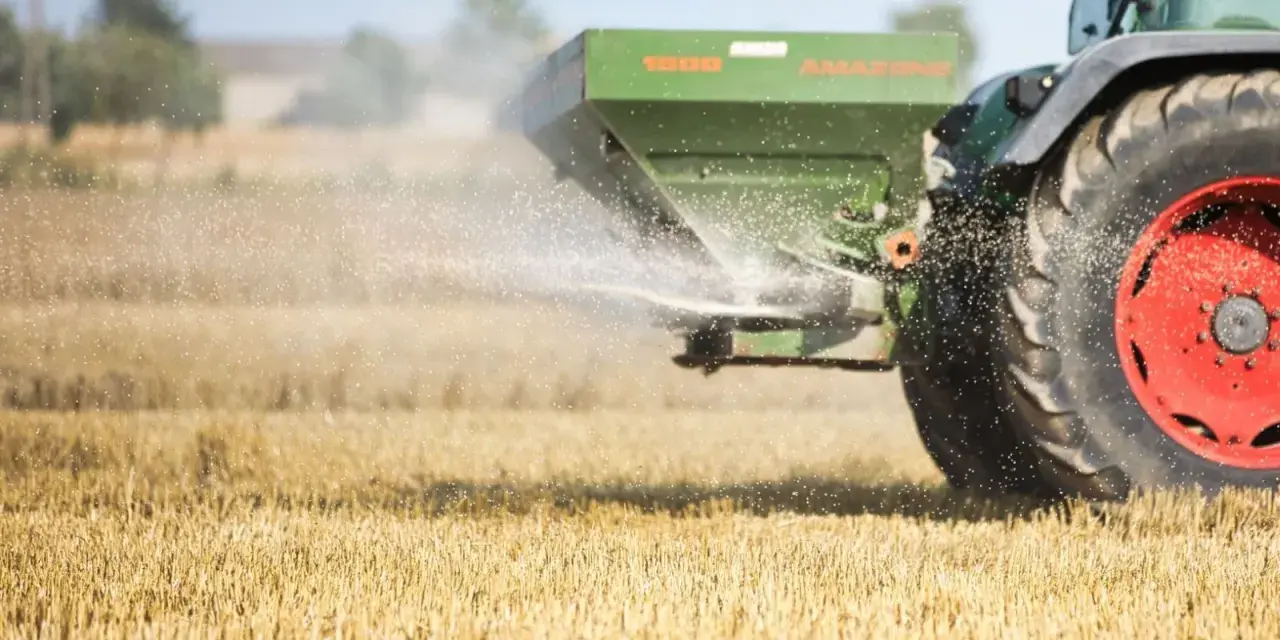 Traktor rozsiewa wapno magnezowe na polu.
