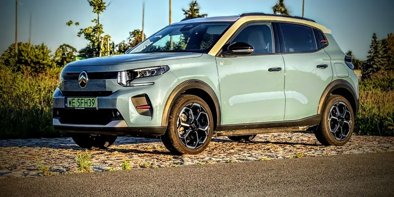 Jasnoszary Citroën ë-C3 z żółtym dachem stoi na tle drzew i nieba.