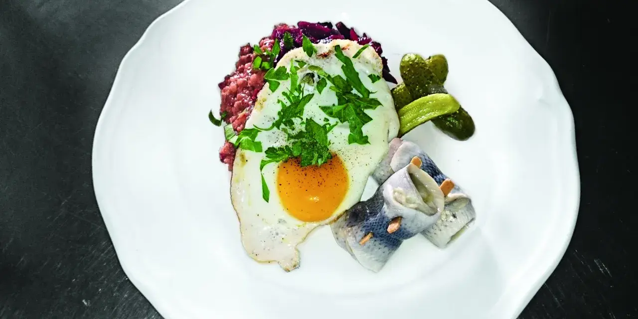Labskaus mit Spiegelei, Rollmops und Gewürzgurken. Die Herkunft dieses norddeutschen Gerichts ist Seefahrer-Tradition.