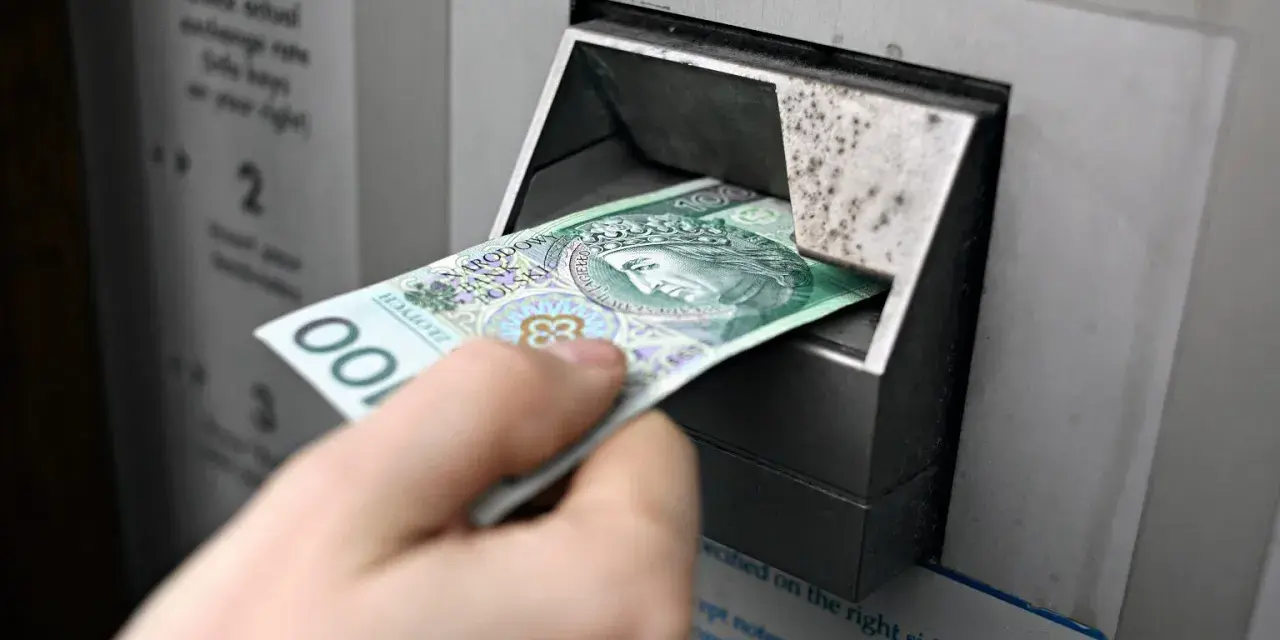 Ręka wkłada banknot 100 zł do bankomatu. Czy państwo może zabrać pieniądze z konta w razie wojny?