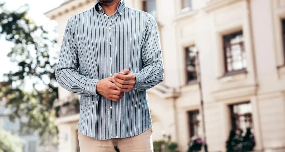 Mężczyzna w paski koszuli, z rękami złożonymi na brzuchu, idealnie pokazuje, kiedy koszula w spodnie tworzy elegancki look.