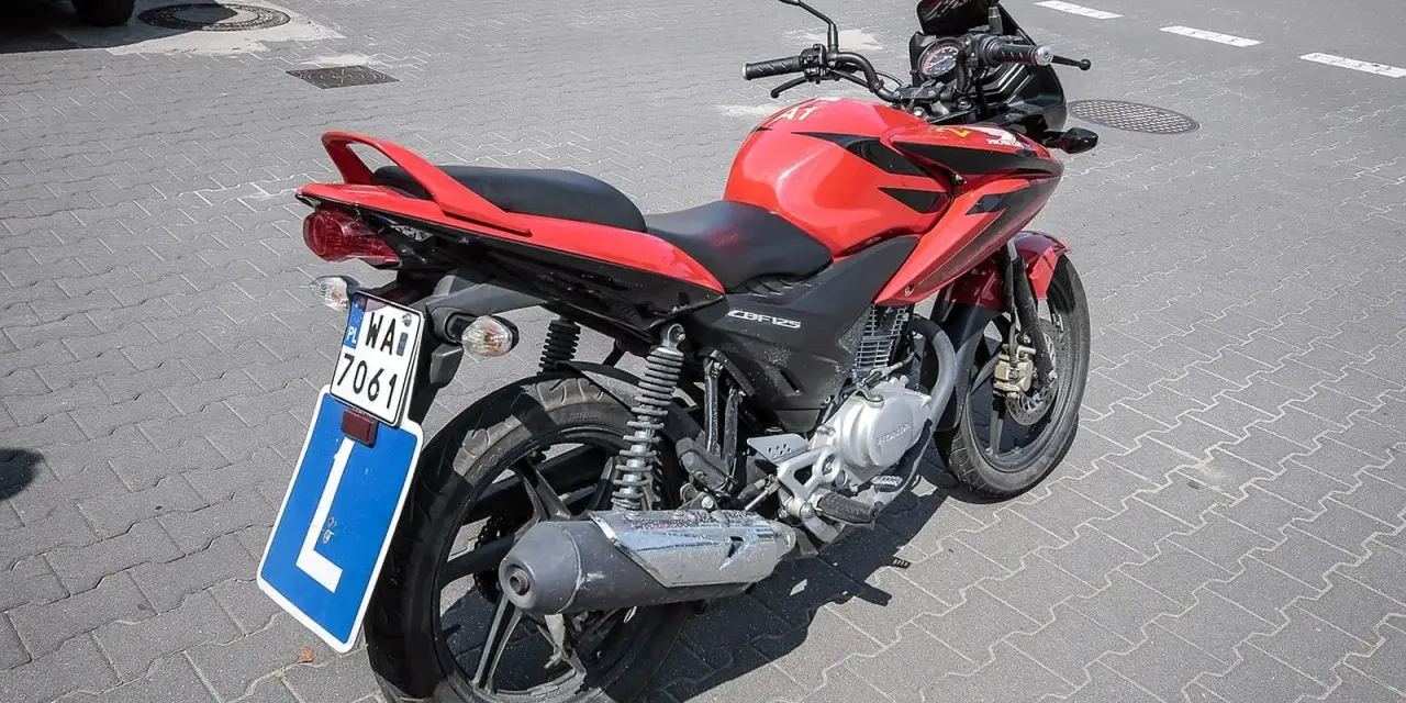 Czerwony motocykl Honda CBF125 z tablicą "L" i numerem rejestracyjnym WA7 7061, gotowy do nauki jazdy na prawo jazdy a1.