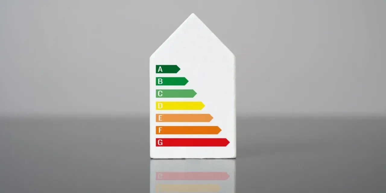 Biały model domu z naklejką klasy energetycznej. Świadectwo energetyczne mieszkania ocenia jego efektywność.