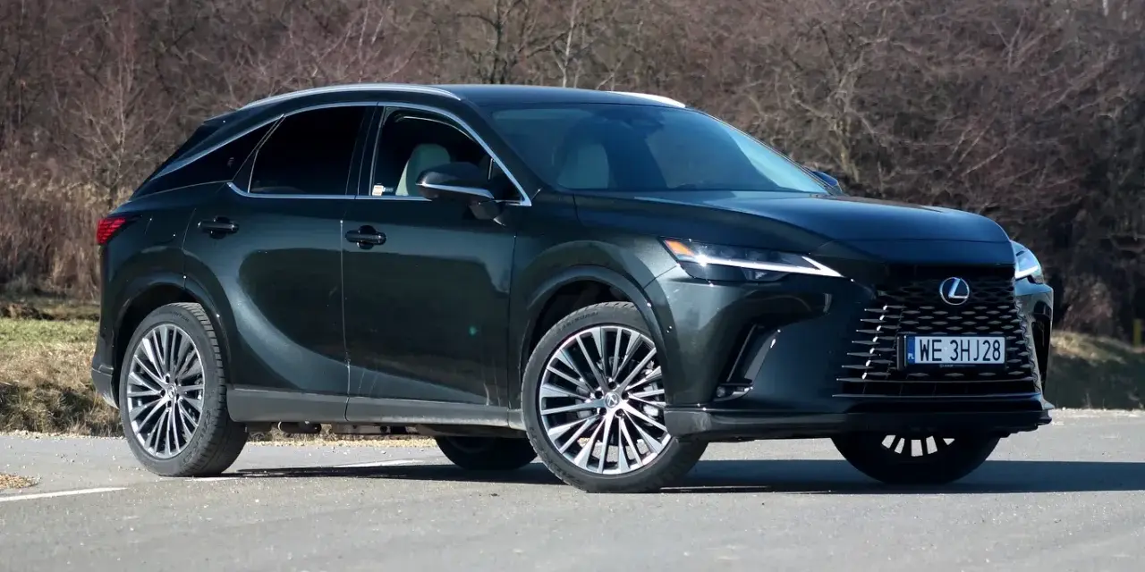 Ciemnozielony Lexus 450h z eleganckimi felgami stoi na drodze, otoczony suchymi krzewami.