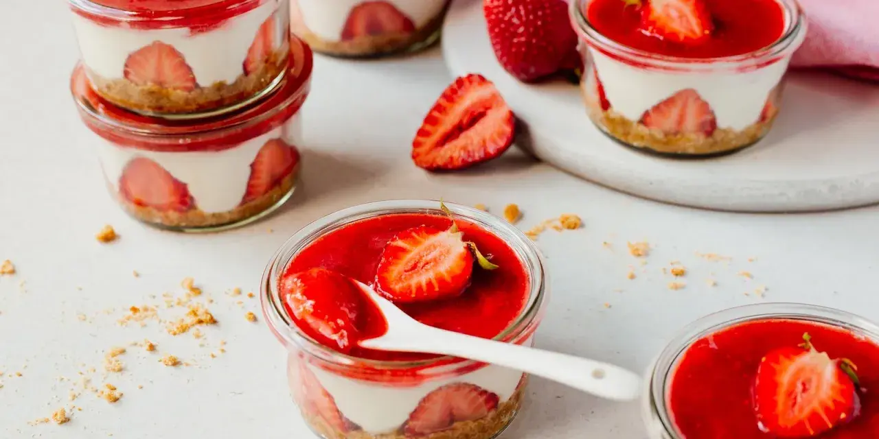 Mehrere kleine Gläser mit einem cremigen Dessert mit Erdbeeren und einer roten Erdbeersauce.