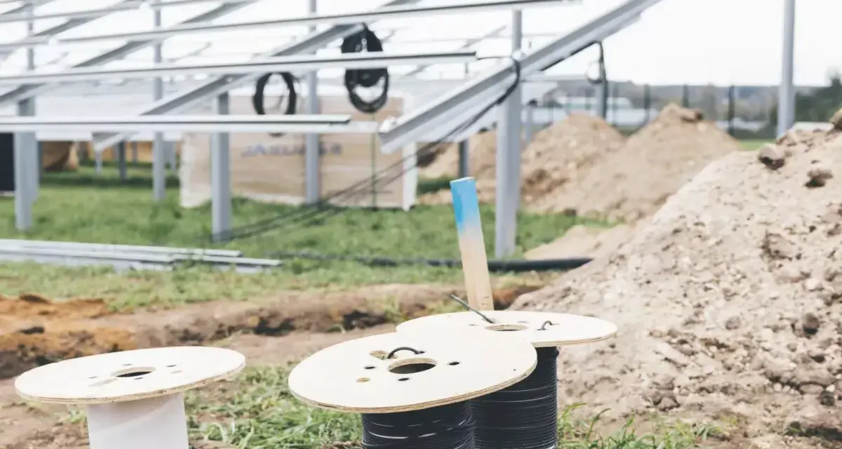 Na placu budowy paneli słonecznych przygotowywane są kable do uziemienia. Widać szpule z przewodami i metalowe konstrukcje.