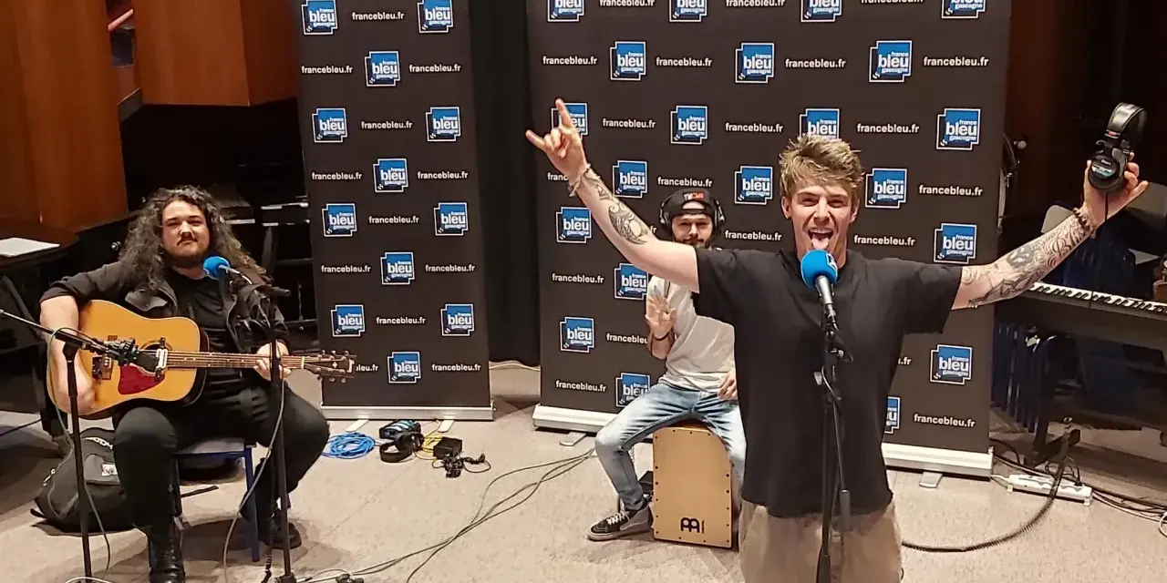 Un groupe rock alternatif français en pleine performance, avec un guitariste, un percussionniste et un chanteur énergique.