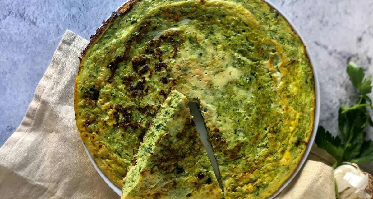 Frittata di zucchine in padella, dorata e profumata, con una fetta tagliata per mostrare la morbidezza interna.