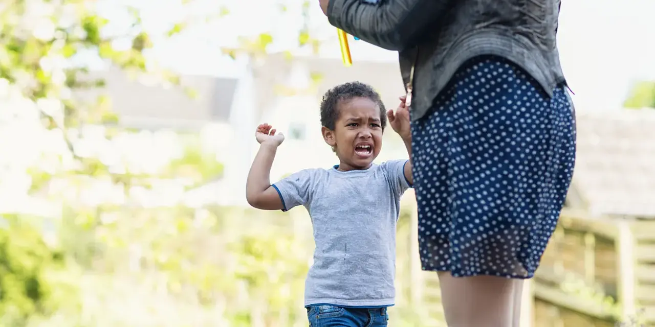 Ein 3-jähriges Kind hat einen Wutanfall, während eine Person Seifenblasen macht.