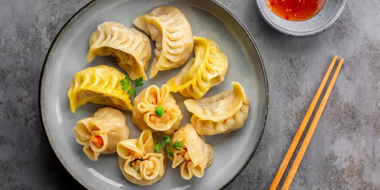 Talerz pełen aromatycznych chińskich pierożków, gotowych do zanurzenia w sosie. Obok pałeczki i miseczka z ostrym dipem.