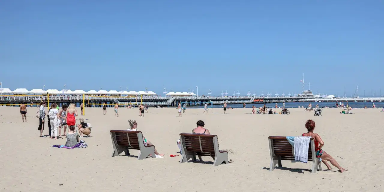 Ludzie odpoczywają na plaży, ciesząc się słońcem i widokiem na molo. To idealne miejsce na polską riwierę.
