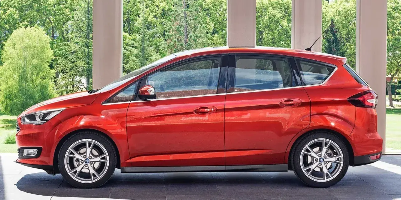 Czerwony Ford C-Max 1.6 benzyna zaparkowany pod arkadami, z zielenią w tle.