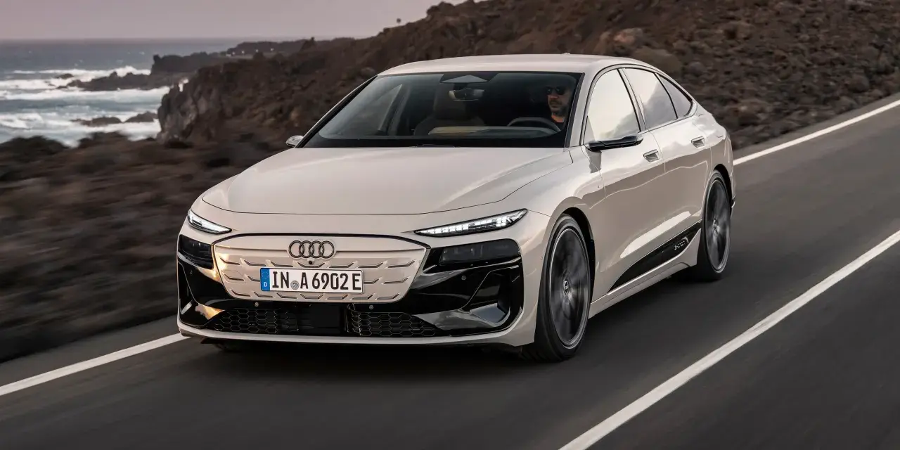 Jasnoszary Audi A6 e-tron jedzie po drodze z widokiem na ocean i góry.