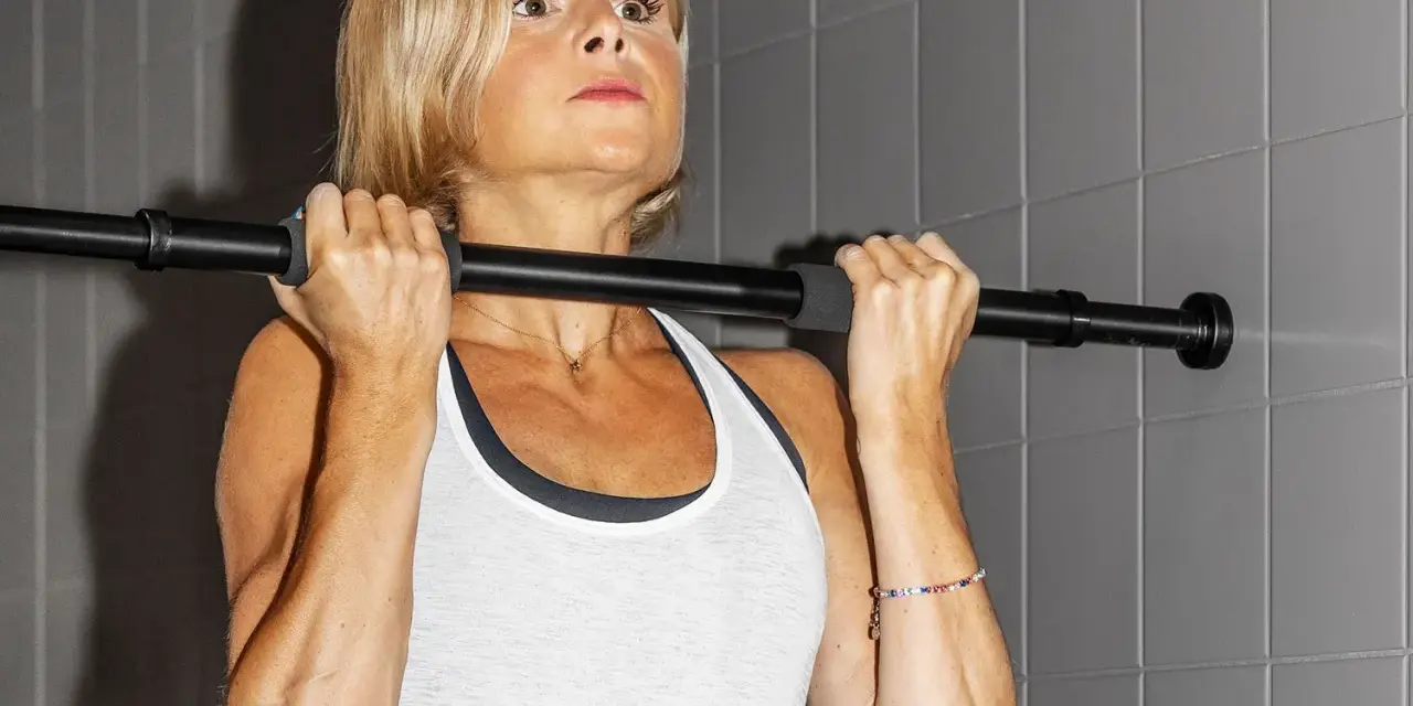 En kvinna med blont hår utför chin ups vid en stång.
