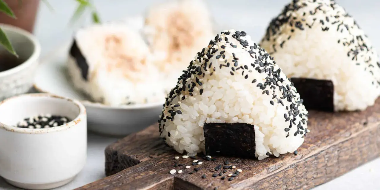 Trójkątne onigiri sushi z czarnym sezamem i kawałkiem nori na drewnianej desce.