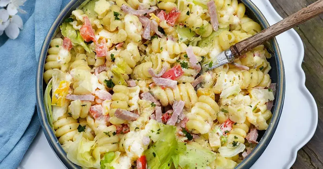 En stor skål med krämig pastasallad med skinka, grönsaker och örter. Perfekt för en sommarlunch!