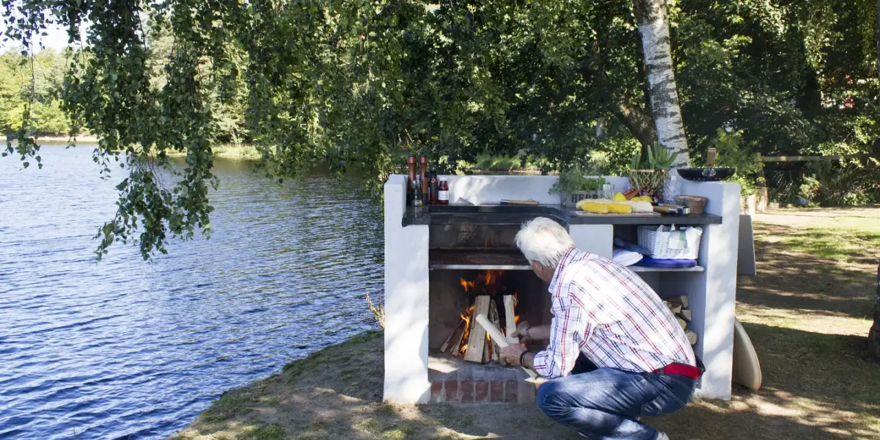 Man tänder en brasa i en nybyggd grill av tegelstenar vid en sjö.