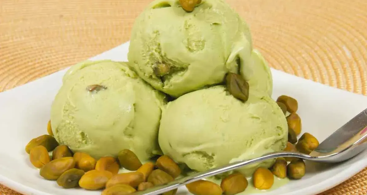 Tre palline di cremoso gelato al pistacchio, guarnite con pistacchi interi, su un piatto bianco con una spolverata di pistacchi tostati.