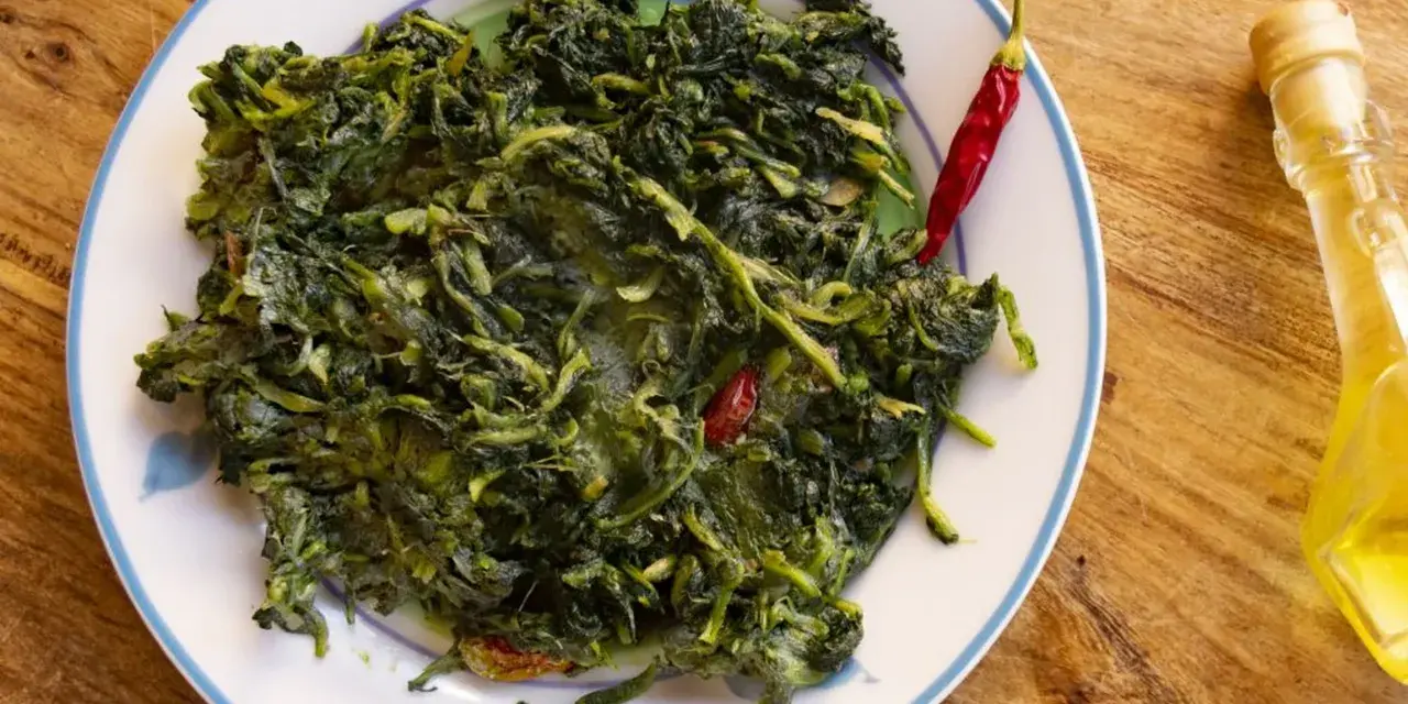 Un piatto di cicoria in padella, condita con peperoncino rosso e un filo d'olio d'oliva, su un tavolo di legno.