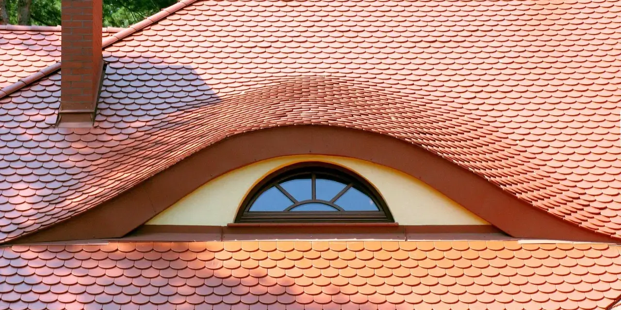 Dachówki ceramiczne w kolorze ceglastym pokrywają dach z charakterystycznym lukarną w kształcie oka.
