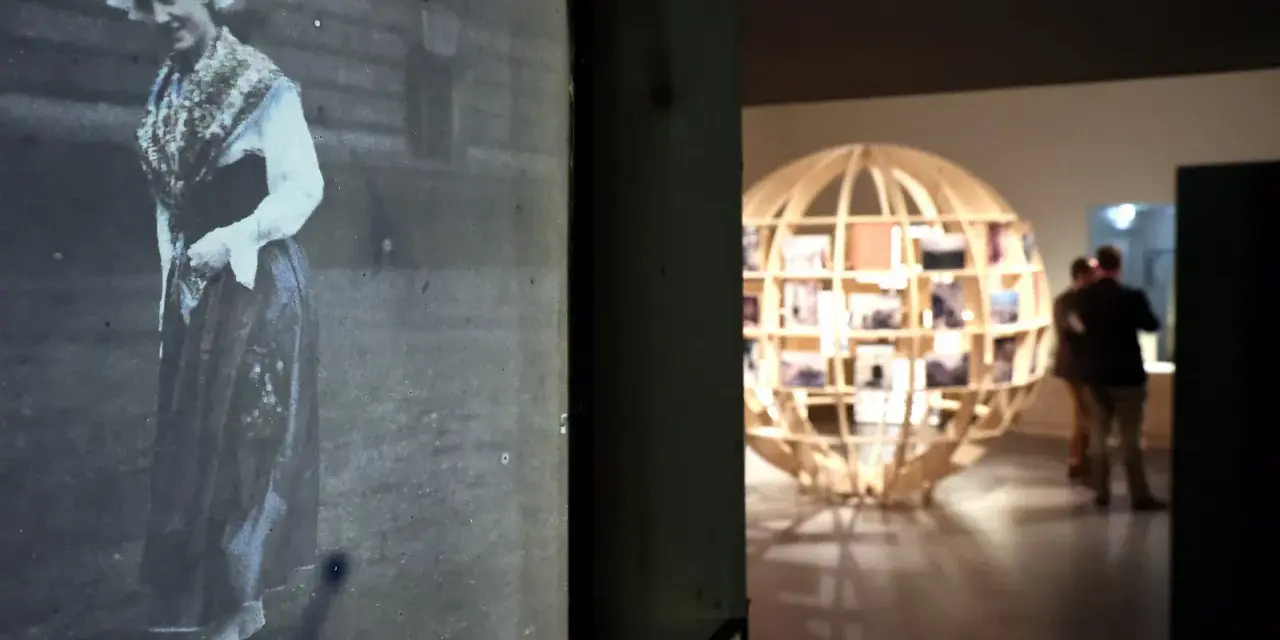 Exposition Albert Kahn : une femme en costume traditionnel sur une photo ancienne, un globe de bois rempli de clichés en arrière-plan.