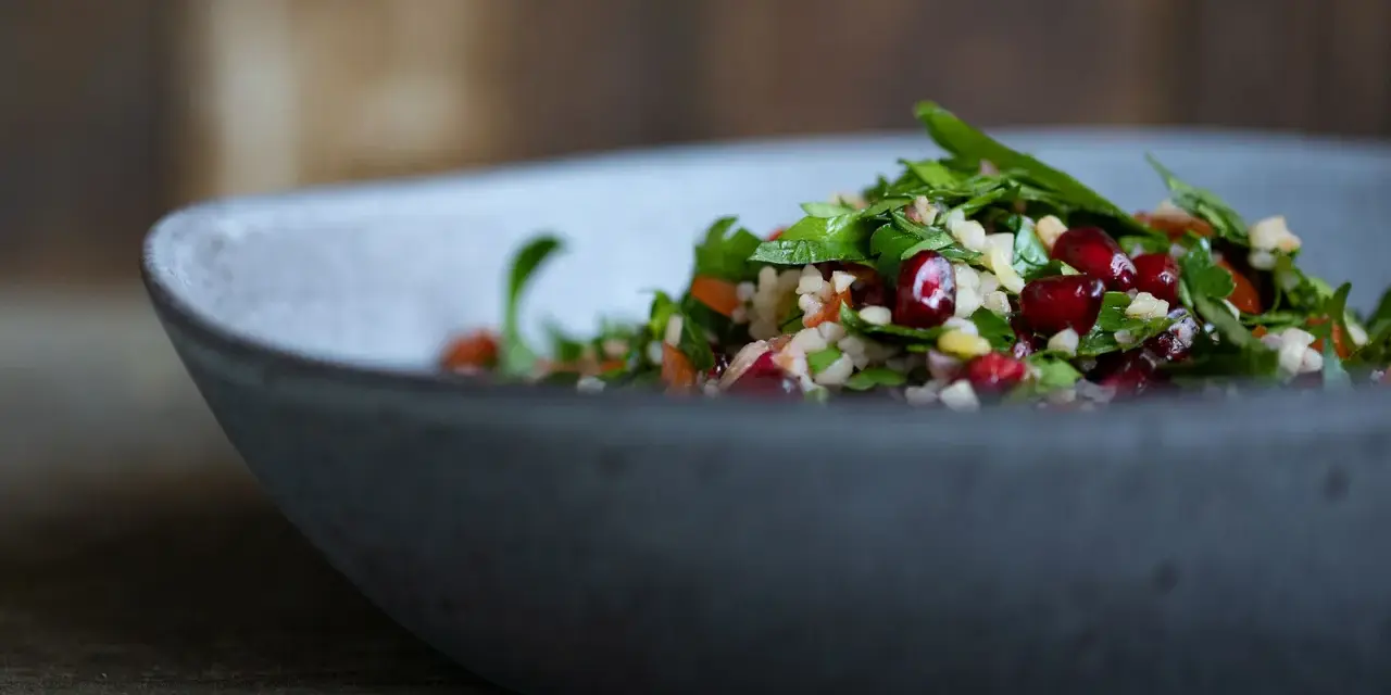Frischer Tabouleh-Salat mit Granatapfelkernen in einer grauen Schüssel. Ein köstliches Rezept für den Sommer.