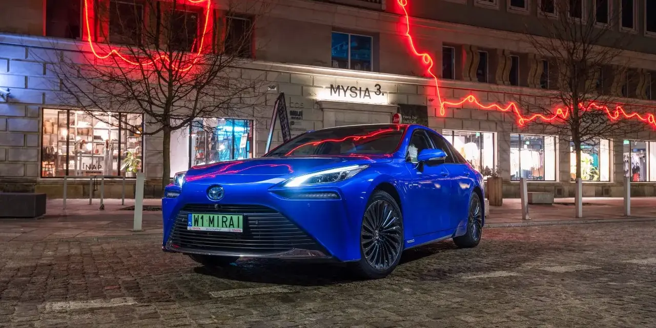 Niebieska Toyota Mirai na nocnej ulicy z neonowym oświetleniem.