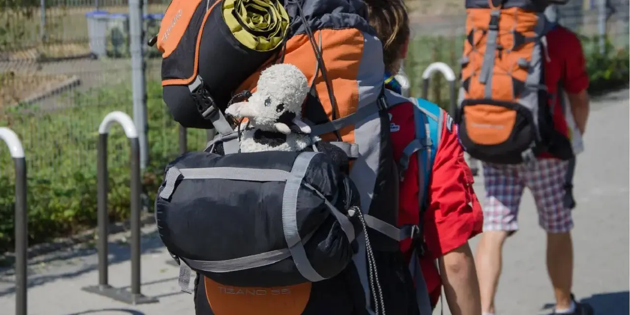 Deux jeunes partent en camp de scout, chargés de leurs sacs à dos. Un doudou mouton est accroché au sac de devant.