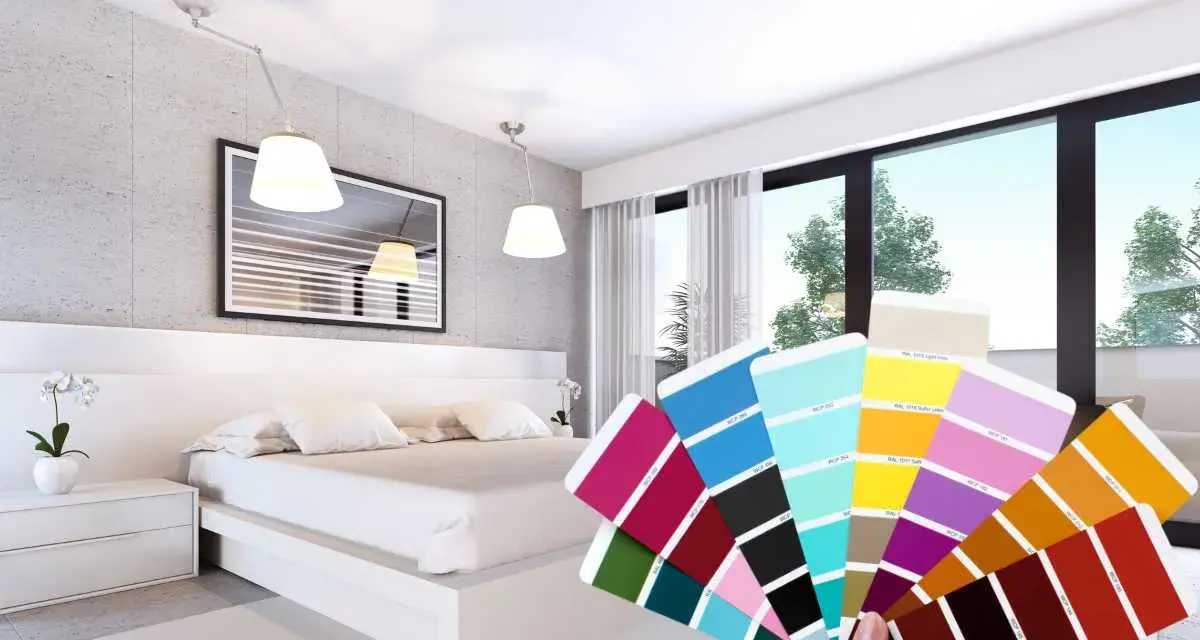 Una mano tiene un campionario di colori davanti a una moderna camera da letto bicolore, con pareti grigie e bianche e un letto bianco.