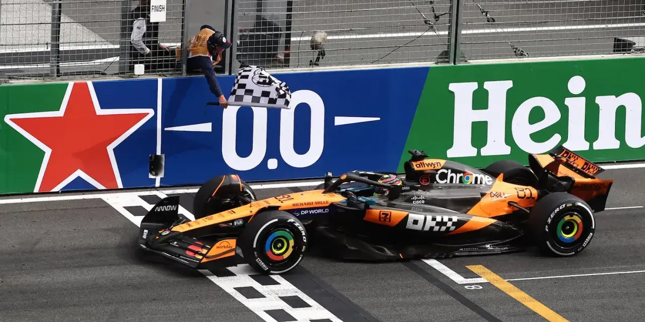 El coche de McLaren cruza la meta en el **Gran Premio Países Bajos**. El piloto celebra la victoria ondeando la bandera a cuadros.