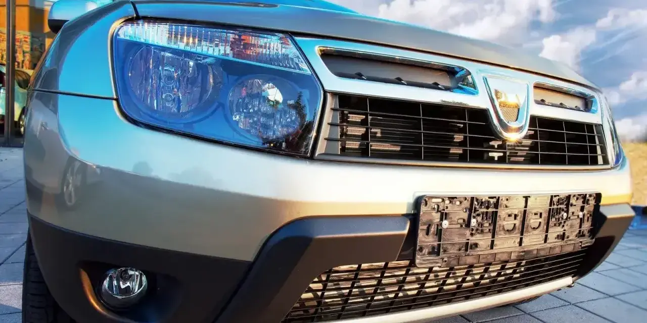 Złoty Dacia Duster 1.6 benzyna z chromowanym grillem i niebieskimi reflektorami, gotowy na przygodę pod błękitnym niebem.