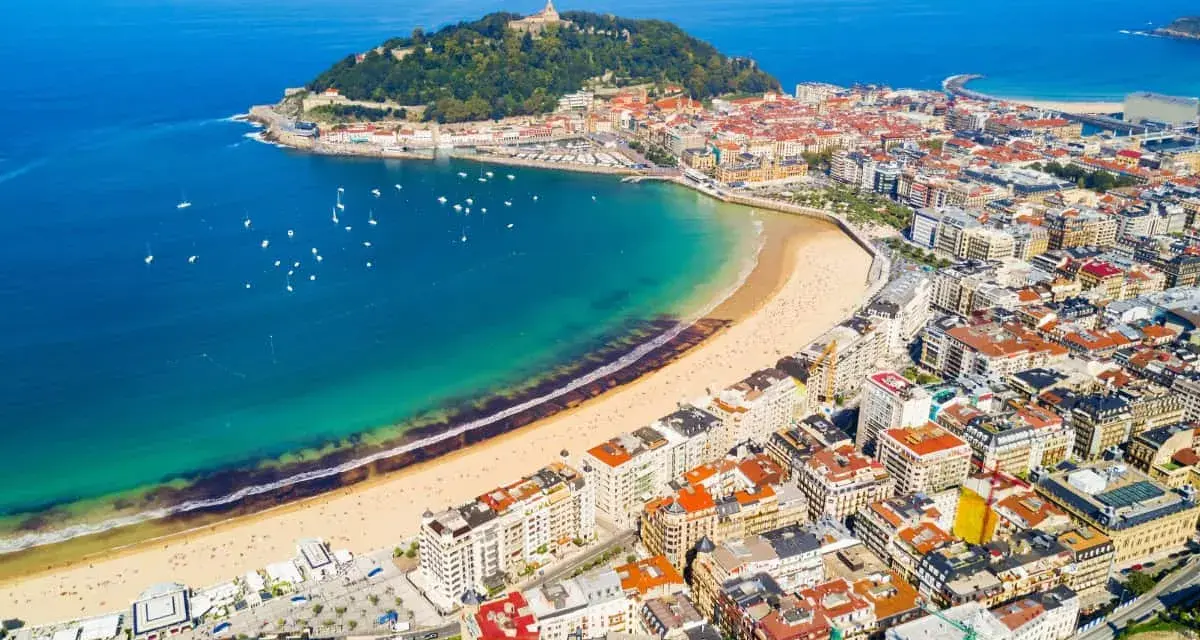 Widok z lotu ptaka na zatokę La Concha w San Sebastian, z piaszczystą plażą, turkusową wodą i zabudową miejską.