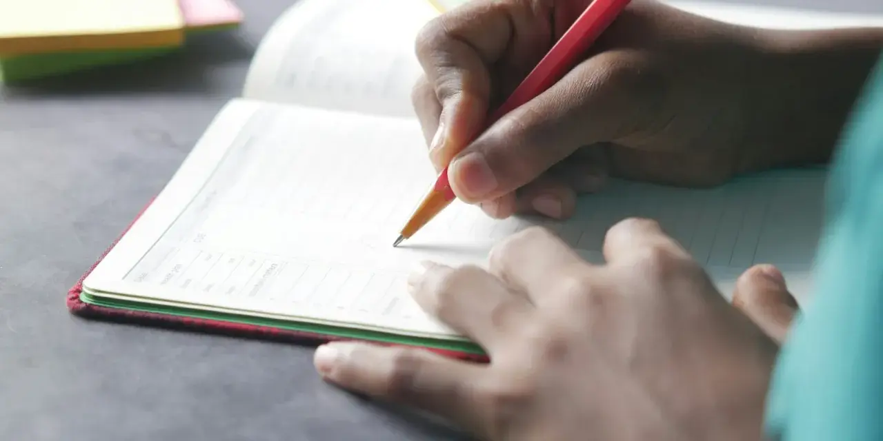 Dłoń pisze w zeszycie, co to dysgrafia? Trudności z pisaniem mogą dotyczyć każdego.